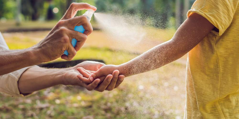 adult sprays bug spray on childs arm